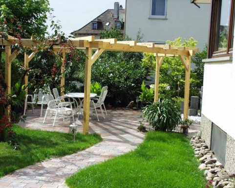 Ein Garten mit Holzpergola, Tisch, Stühlen und grünen Pflanzen, umgeben von Rasen.