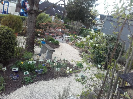 Friedlicher Garten mit Wegen, Blumenbeeten und Bäumen.