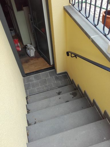 Treppenhaus mit grauen Stufen und einem Handlauf, Blick auf den Ausgang.