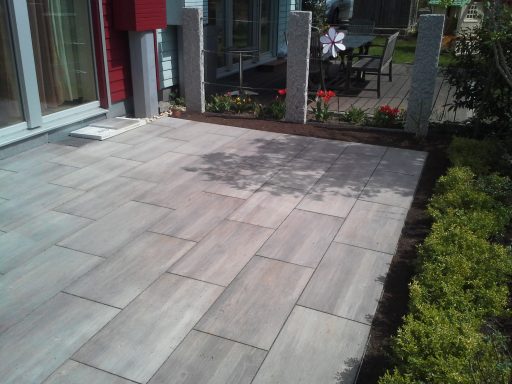 Gepflasterte Terrasse mit Blumenbeet und modernen Zaunpfosten.