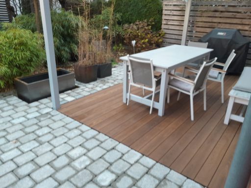 Holzterrasse mit Tisch, Stühlen und Pflanzen, umgeben von grauen Steinen.